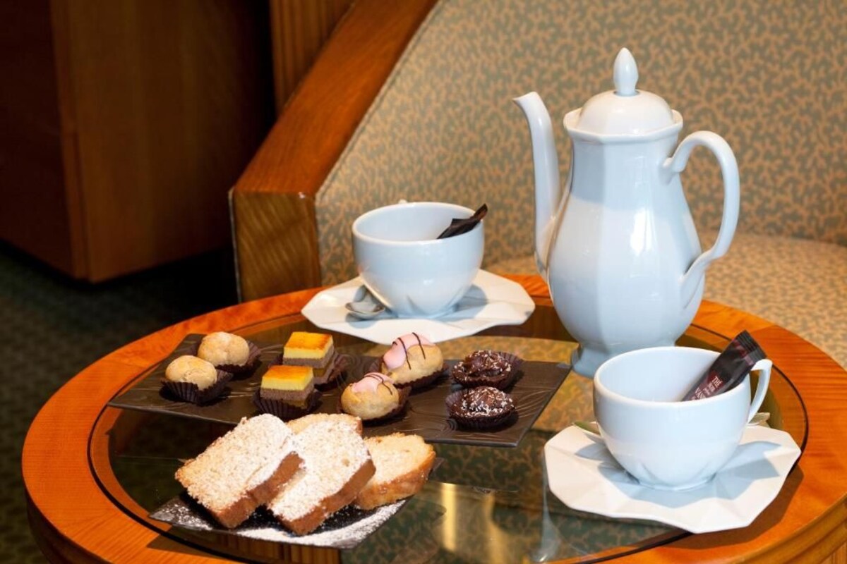 Una mesa con un calentador de té, dos tazas y una variedad de pasteles y sándwiches.