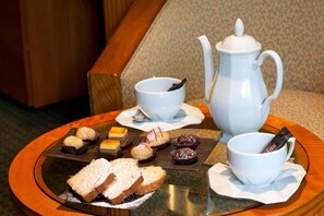 Una mesa con un calentador de té, dos tazas y una variedad de pasteles y sándwiches.