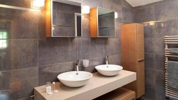 A modern bathroom with two large white sinks, a wooden vanity, and a built-in mirror.