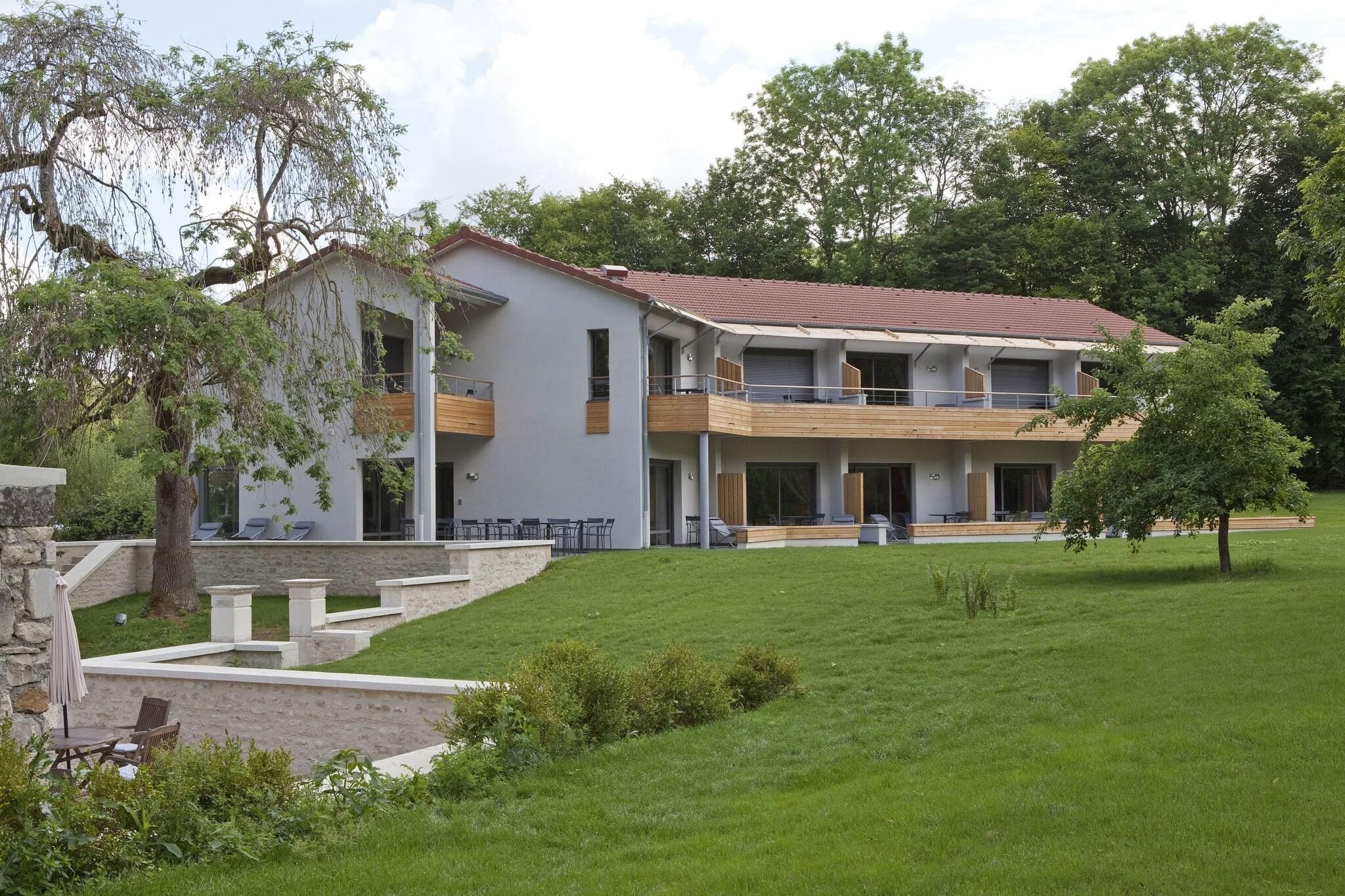 Een modern gebouw met twee verdiepingen, balkons, een overdekt terras en een verzorgd gazon.