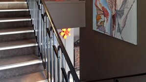 Una escalera con barandilla metálica, una lámpara decorativa roja y un cuadro abstracto grande en la pared.