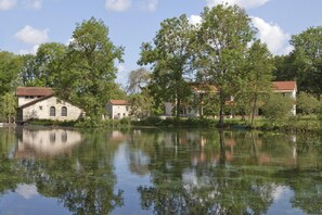 A serene lakeside scene with stone buildings and lush greenery. - Logis Hotel la Source Bleue (Gudmont)