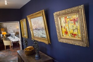 Una stanza con due quadri appesi al muro, una statua su un tavolo, e in secondo piano un'area pranzo con tavolo e sedie.
