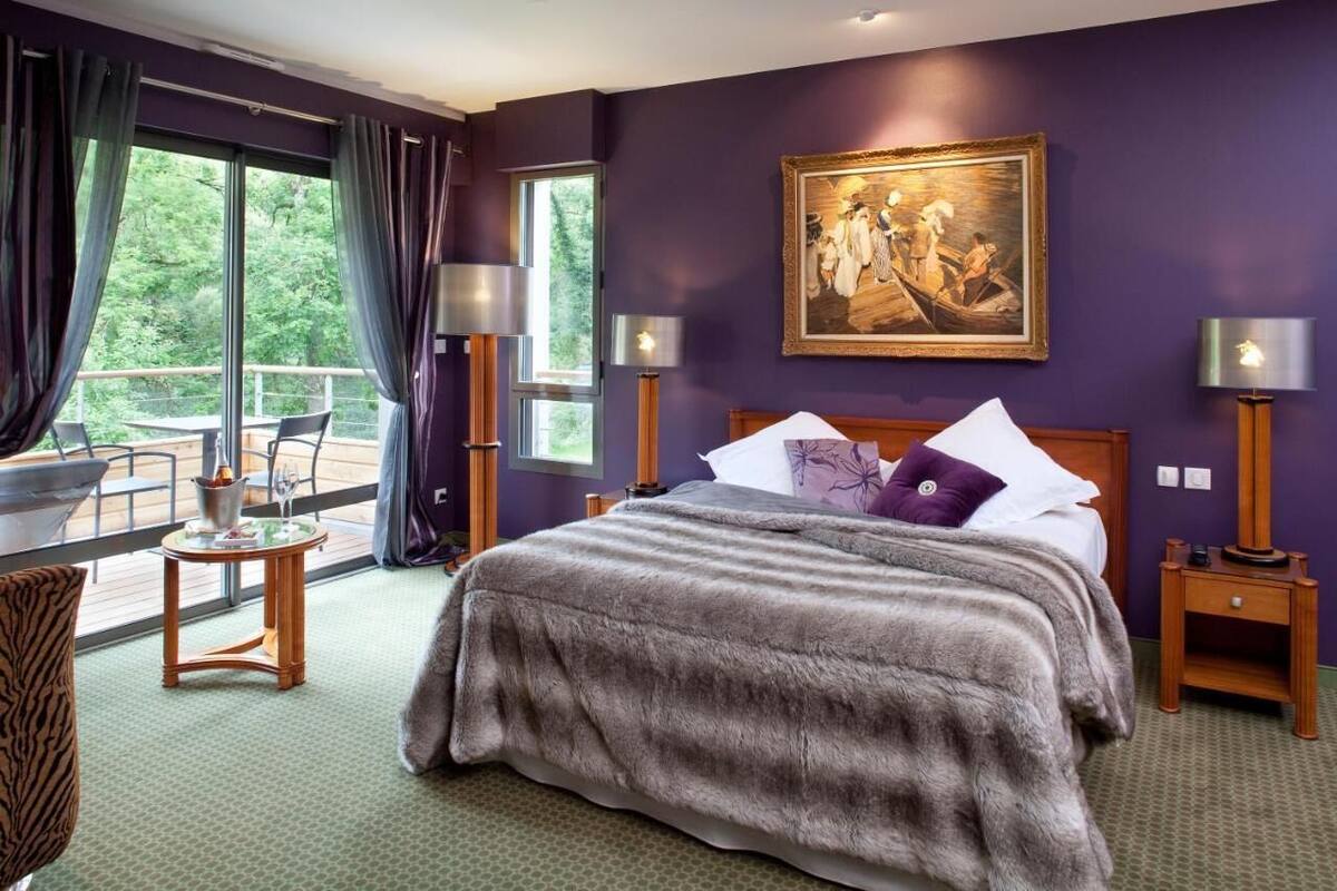 A bedroom with a large bed, a painting on the wall, and a balcony with a table and chairs.