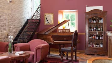 Une pièce avec un grand piano, une bibliothèque contenant des bouteilles d’alcool, un escalier et un sol recouvert d’une moquette rouge.
