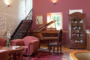 Una habitación con un piano de cola, una estantería llena de licores, una escalera y un suelo cubierto de alfombra roja.