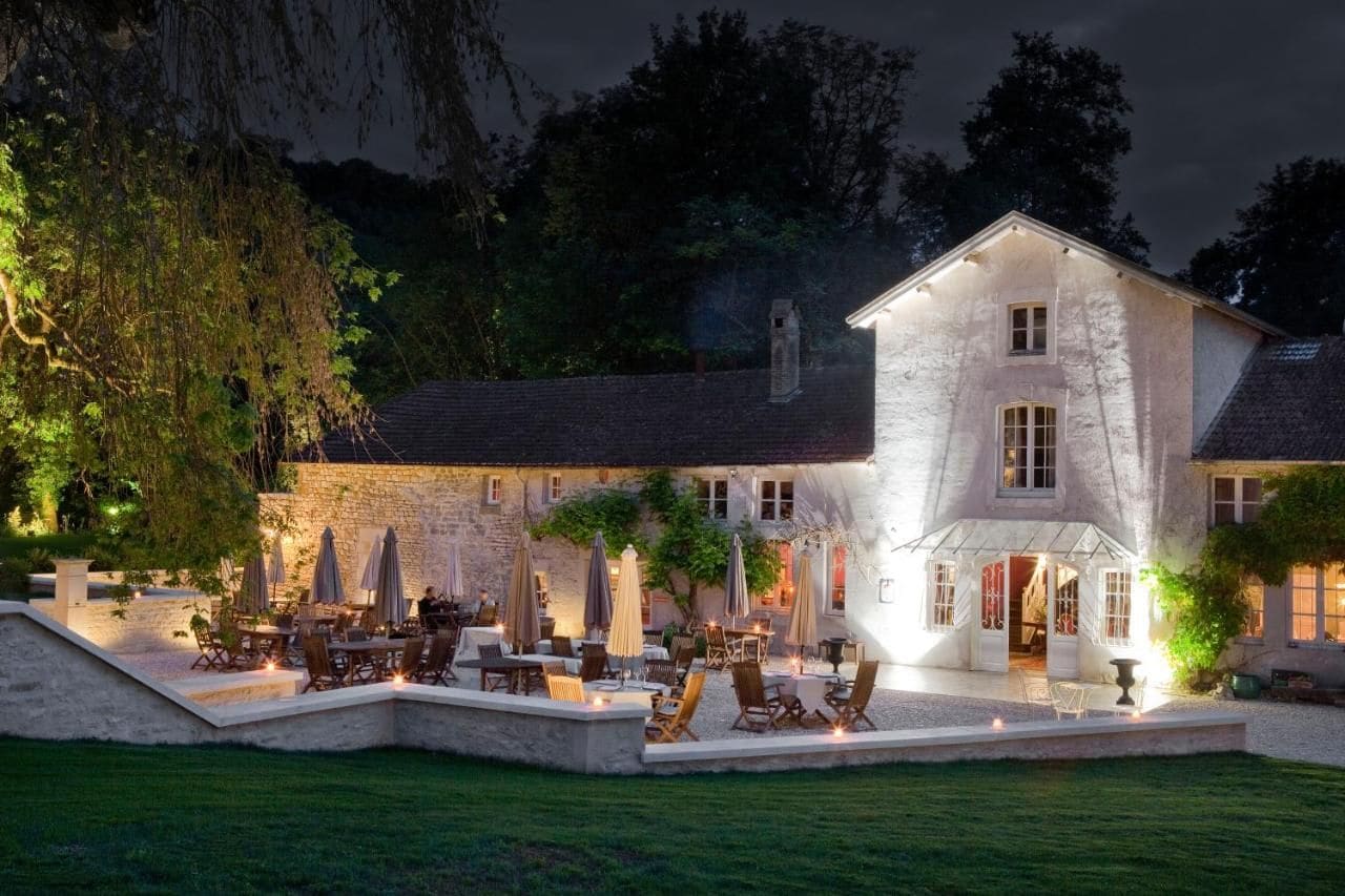 A stone building with a large patio area, outdoor seating, and a well-lit entrance.