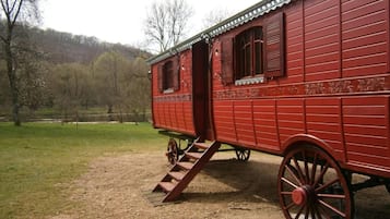 A red wooden carriage with a ramp leading up to the entrance, set in a grassy field with trees in the background.