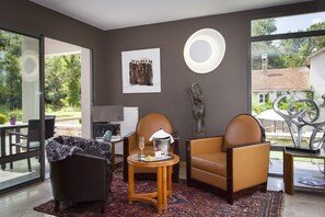 A modern living room with a large window, a fireplace, and a dining area with a table and chairs. - Logis Hotel la Source Bleue (Gudmont)