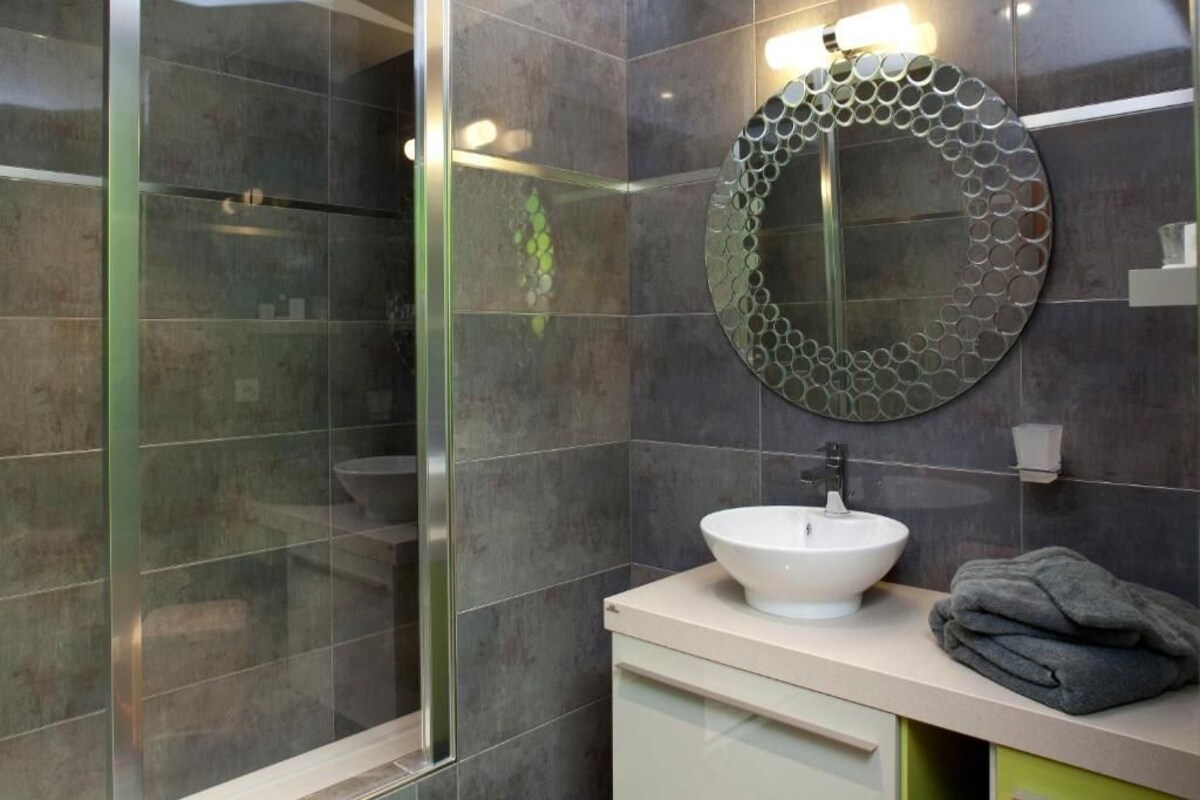 Un baño moderno con cabina de ducha de vidrio, un espejo redondo con diseño circular y un lavamanos blanco sobre encimera beige.