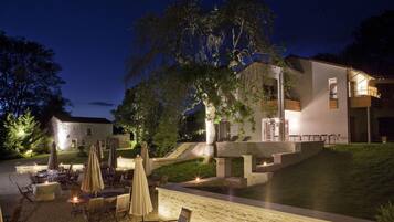 A modern outdoor dining area with tables and umbrellas, a stone pathway, and a building with a balcony.