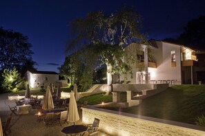 A modern outdoor dining area with tables and umbrellas, a stone pathway, and a building with a balcony. - Logis Hotel la Source Bleue (Gudmont)