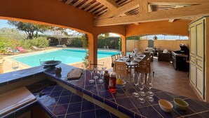 Un espace de restauration en plein air avec vue sur la piscine, un plafond en bois et un sol carrelé.