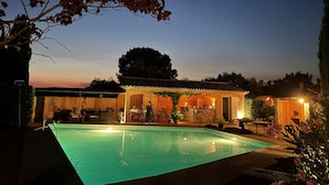 Une piscine avec un espace patio, un bar et un coin salon abrité.