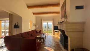 Un salon avec un canapé rouge, une cheminée et une vue sur l’extérieur, visible à travers une porte vitrée.