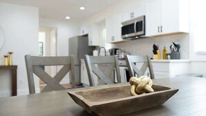 A modern kitchen with white cabinets, a microwave, and a wooden table with a salt and pepper shaker. - Beautifully Modern Cottage in Historic Norcross (Norcross)