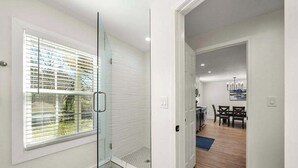 A modern interior with a glass shower, a dining area with a table and chairs, and a kitchen in the background. - Beautifully Modern Cottage in Historic Norcross (Norcross)