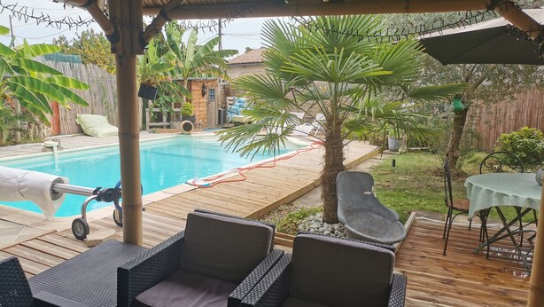 A covered outdoor area with a pool, wicker furniture, and a wooden deck. - Maison Pierre 9 Couchages Piscine Chauffée Jacuzzi (Abzac)