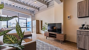 Ein modernes Wohnzimmer mit großem Fernseher, Holzmöbeln und Blick auf die Stadt durch große Fenster.