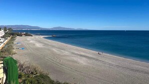 Ein weiter Sandstrand, ein klarer blauer Himmel, ruhige See und entfernte Berge.