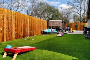 A backyard with artificial grass, a wooden fence, a trampoline, and a covered seating area.
