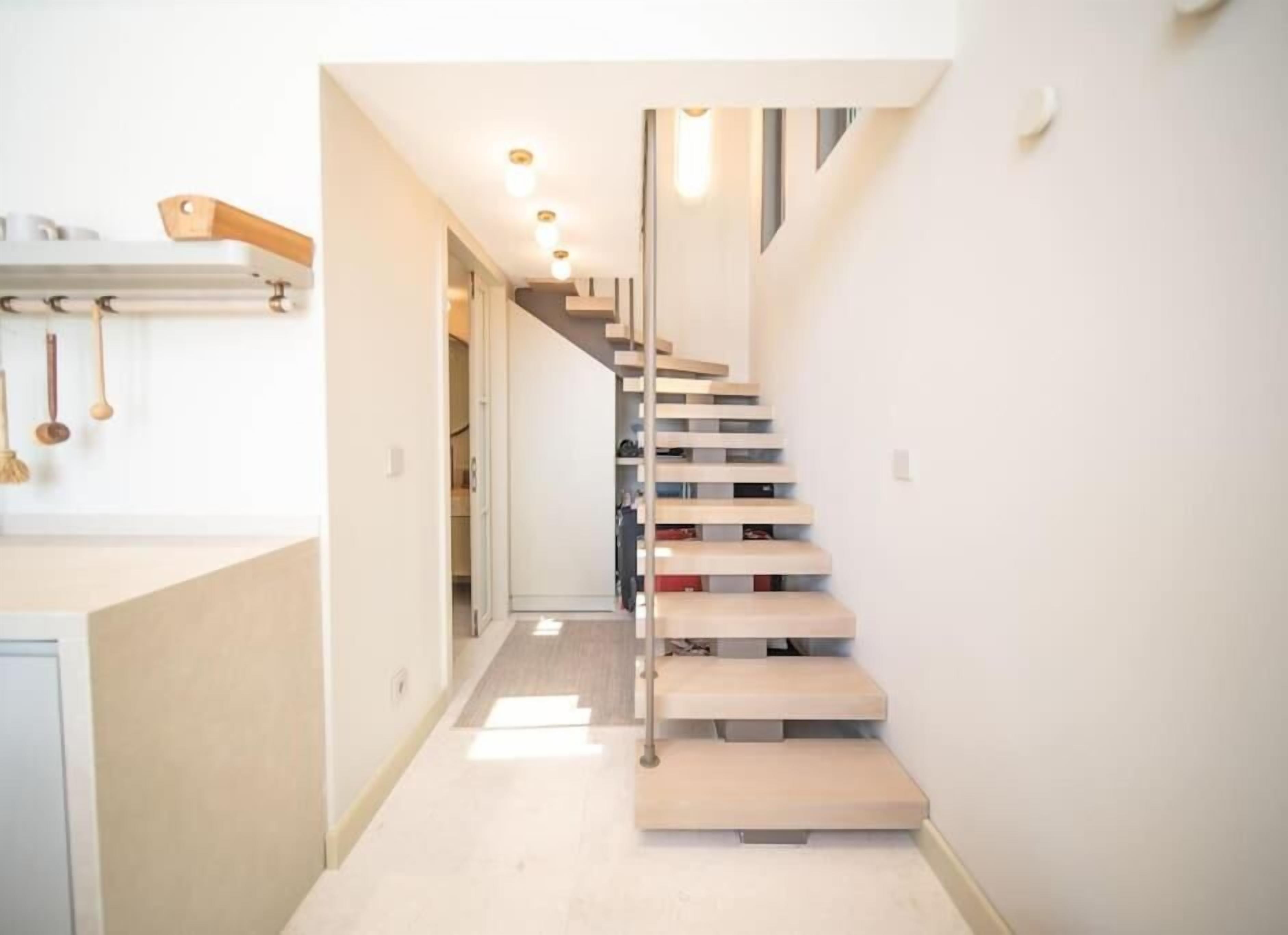 A modern interior with a minimalist staircase, a kitchen area with wooden utensils, and a clean, bright design.