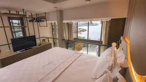 Et hotelværelse med en stor seng, et fjernsyn, en balkon med havudsigt og en hængende lampe.