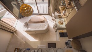 Et moderne interiør med en hvid sofa, en hængende lampe og et køkken med diverse apparater og redskaber.