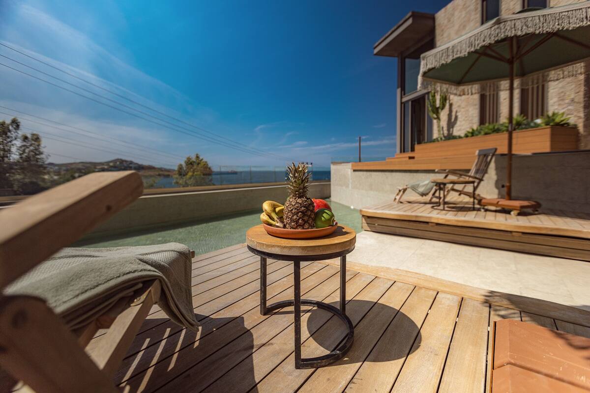 Eine Holzterrasse mit einem Tisch voller Obst, einem Pool und einem modernen Gebäude mit Balkon.