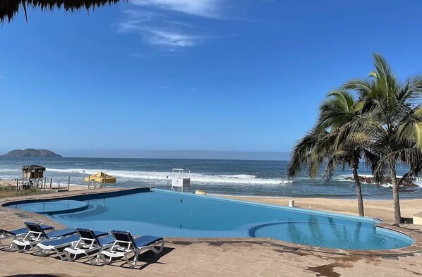 Piscina con sillas de descanso, un puesto de socorrista y vista al mar.