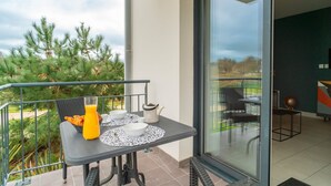 Ein Balkon mit Tisch, gedeckt für das Frühstück, darunter eine Schüssel mit Müsli, ein Glas Orangensaft und ein Teekessel.