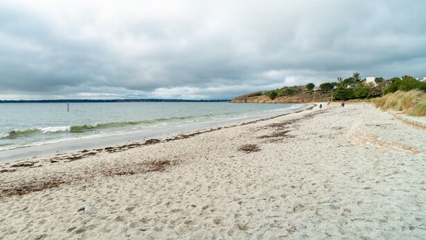 Ein Strand mit sandigem Ufer, einige Personen in der Ferne und ein bewölkter Himmel.