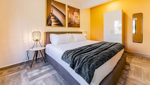 Una habitación de hotel moderna con una cama grande, piso de madera, un armario y un espejo fijado a la pared.
