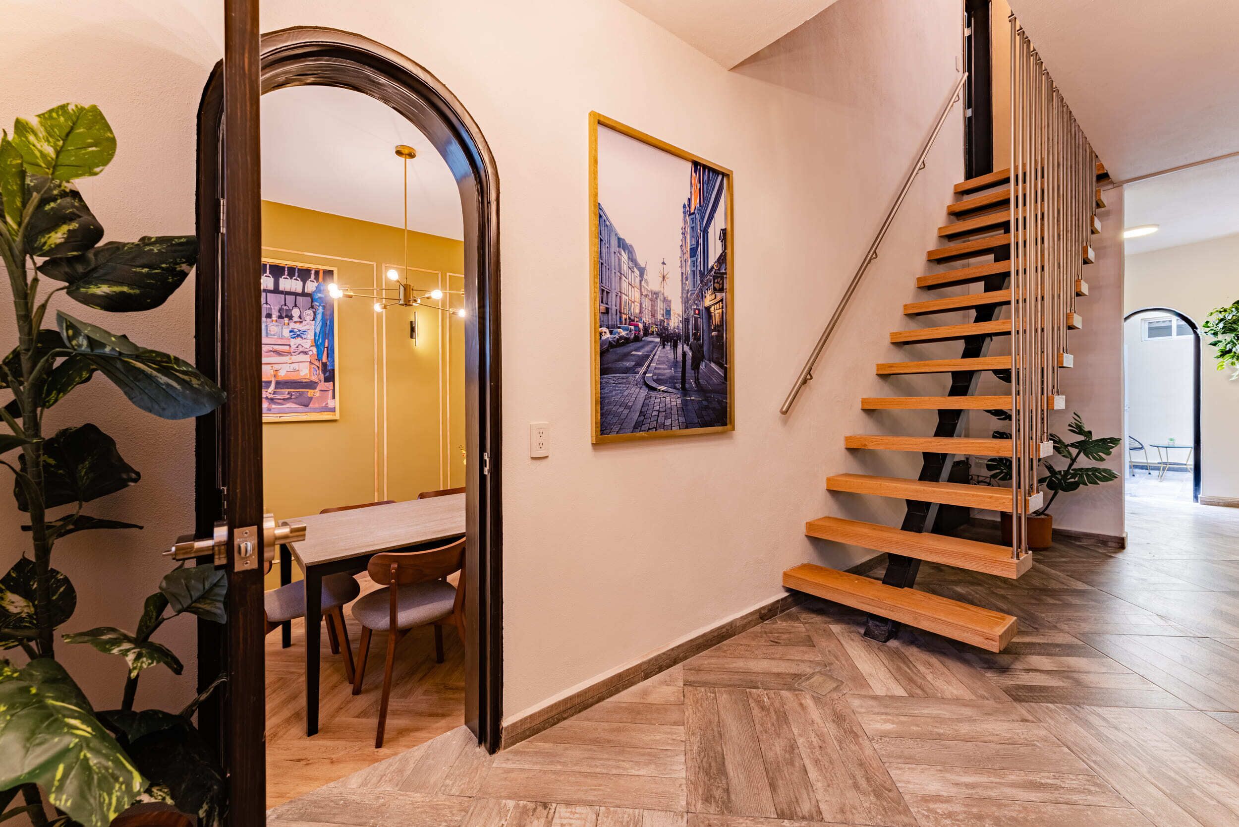 A modern interior with a wooden staircase, a dining area, and a hallway leading to another room.