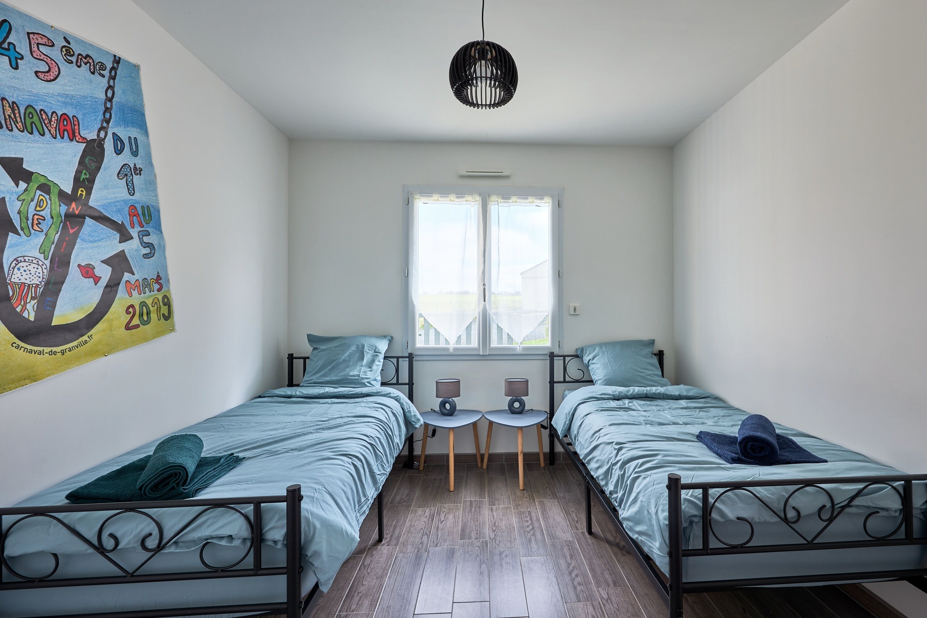 A room with two beds, a window, a small table, and a wall decoration.