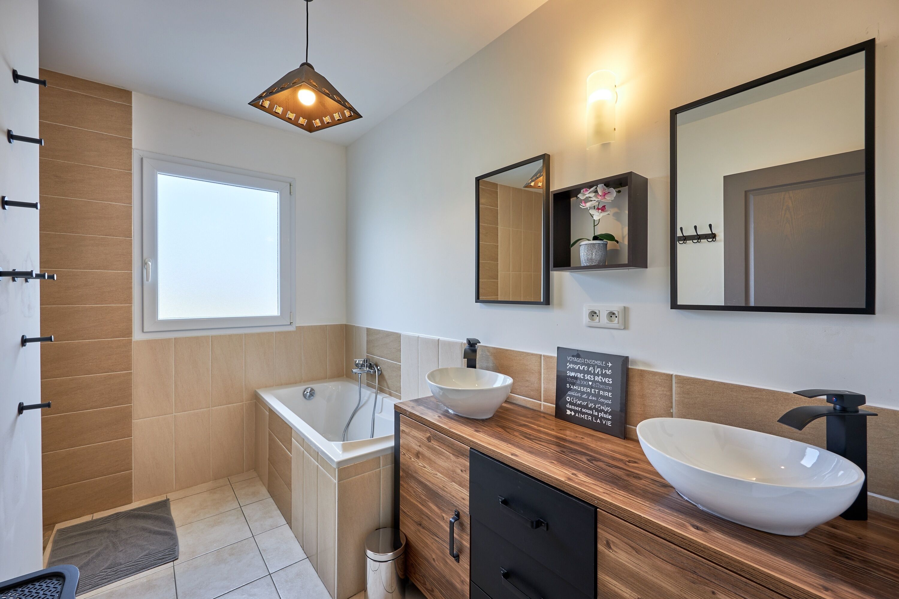 Ein modernes Badezimmer mit einer Badewanne, zwei Waschbecken, einer Holzausstattung und einem großen Spiegel.