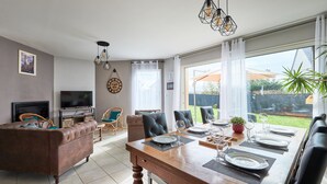 A dining area with a wooden table set for four, a television, and a sofa in the background.