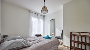 A bedroom with a bed, a bedside table, a mirror, a hanging light fixture, and a wooden shelf.