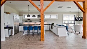 A spacious kitchen with white cabinets, a central island, blue bar stools, and wooden beams.