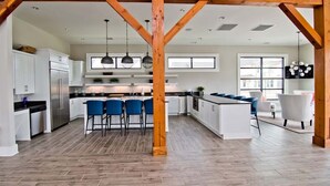 A spacious kitchen with white cabinets, a central island, blue bar stools, and wooden beams. - Pirate Haven, Soundside House in Beaufort, NC! (Beaufort)
