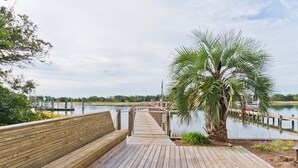 A wooden boardwalk leading to a dock over water, with a palm tree and benches along the path.