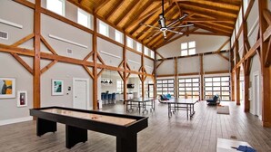 A spacious indoor area with a pool table, ping pong tables, and a ceiling fan.