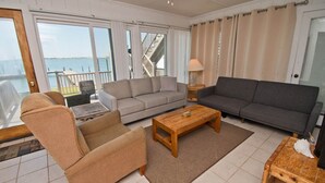A spacious living area with a sofa, armchair, and coffee table, large windows with a view of the sea, and a balcony with a railing. - Speight House, Soundfront House in Historical Beaufort, NC! (Beaufort)