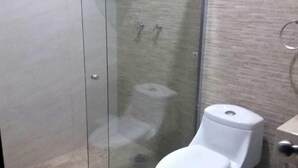 Un baño moderno con ducha envuelta en vidrio, inodoro blanco y un pequeño cubo de basura.