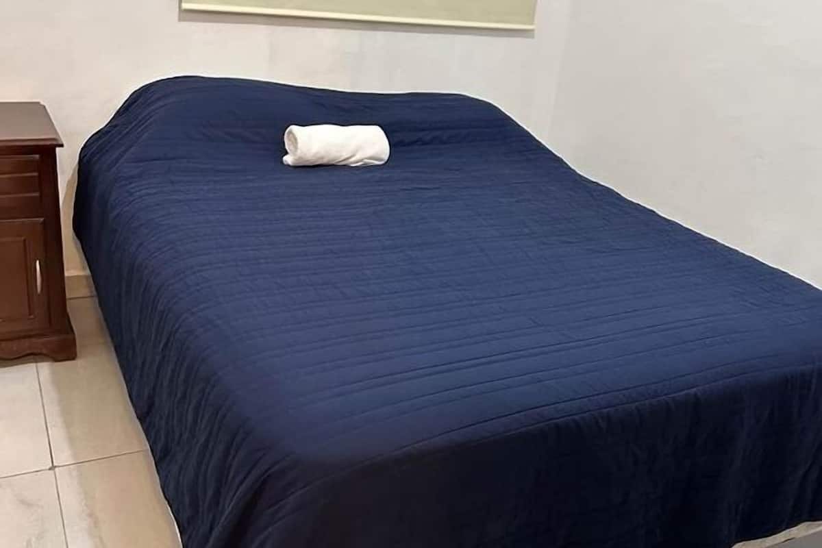 Una cama individual con un edredón azul oscuro y una toalla blanca.