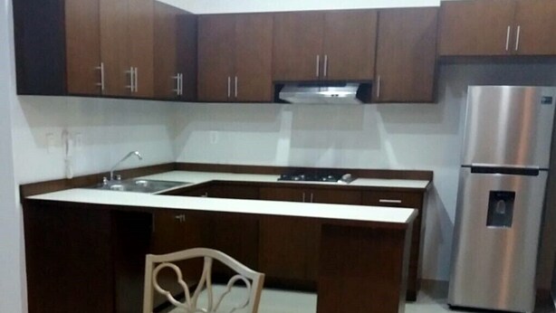 Una cocina con armarios de madera oscura, un refrigerador de acero inoxidable y una encimera blanca.