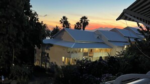 Uma casa moderna com varanda, cercada por vegetação e palmeiras, ao pôr do sol.