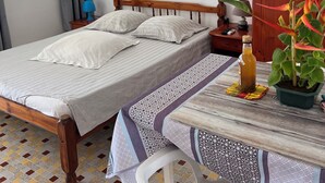 Cama bem arrumada com um jogo de mesa estampado, luminária de cabeceira, garrafa de suco de laranja e planta em vaso.
