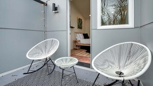 Ein modernes Zimmer mit großem Fenster, einem Bett mit weißem Kopfteil und zwei weißen Stuhlgestellen.