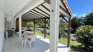 Ein überdachter Außenbereich mit Terrassentisch und -stühlen, einer Holzpergola und Blick auf Garten und Straße.